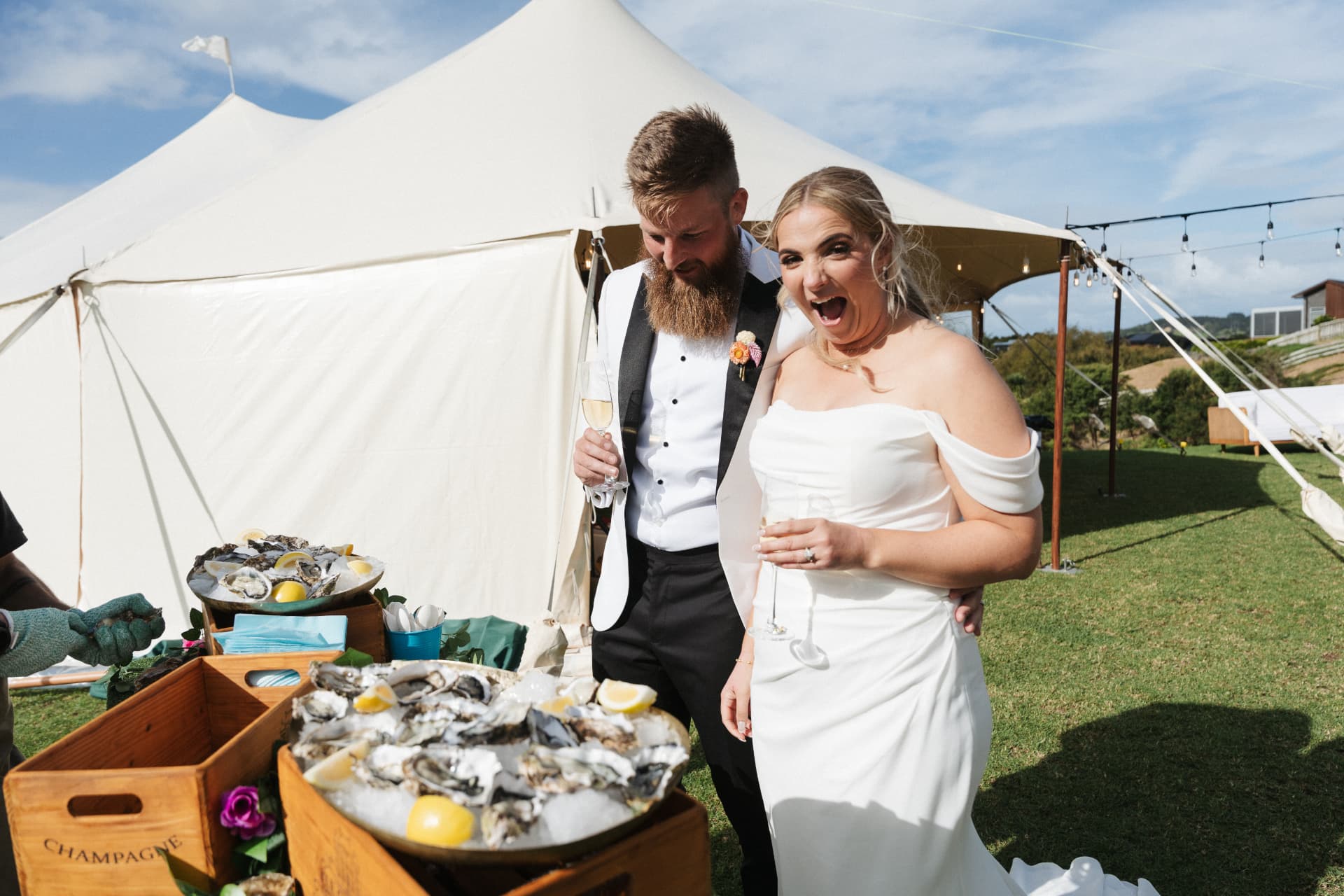 Bride and groom with champagne beside The Oyster Bar Co. mobile oyster bar at a marquee wedding